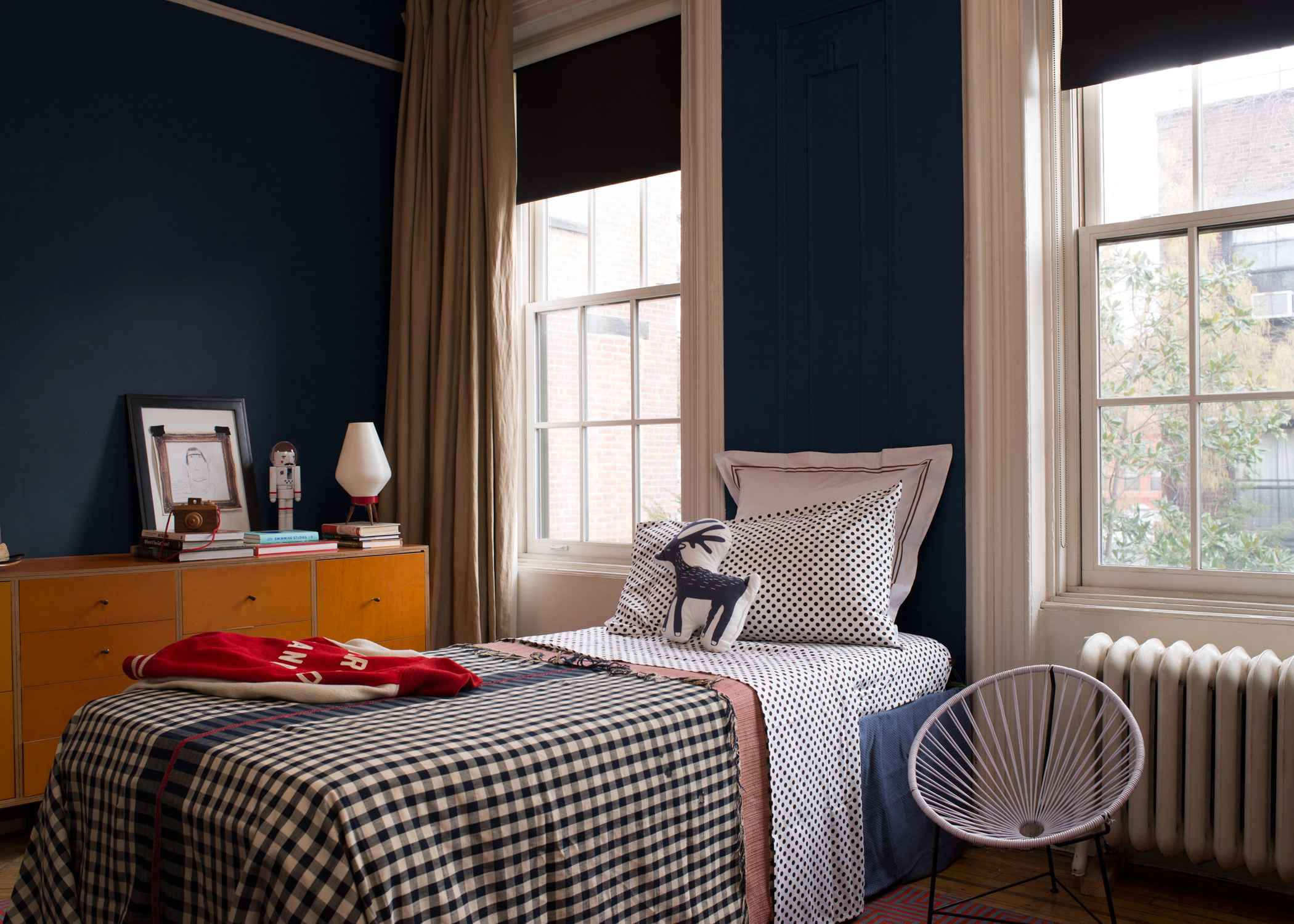 Mid-century modern chair with wooden legs and colorful patchwork upholstery, set against a dark blue wall.