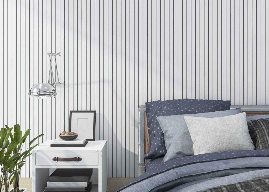 Modern bedroom with vertical striped wallpaper, navy and gray bedding, and a white nightstand topped with books, a bowl, and framed art.