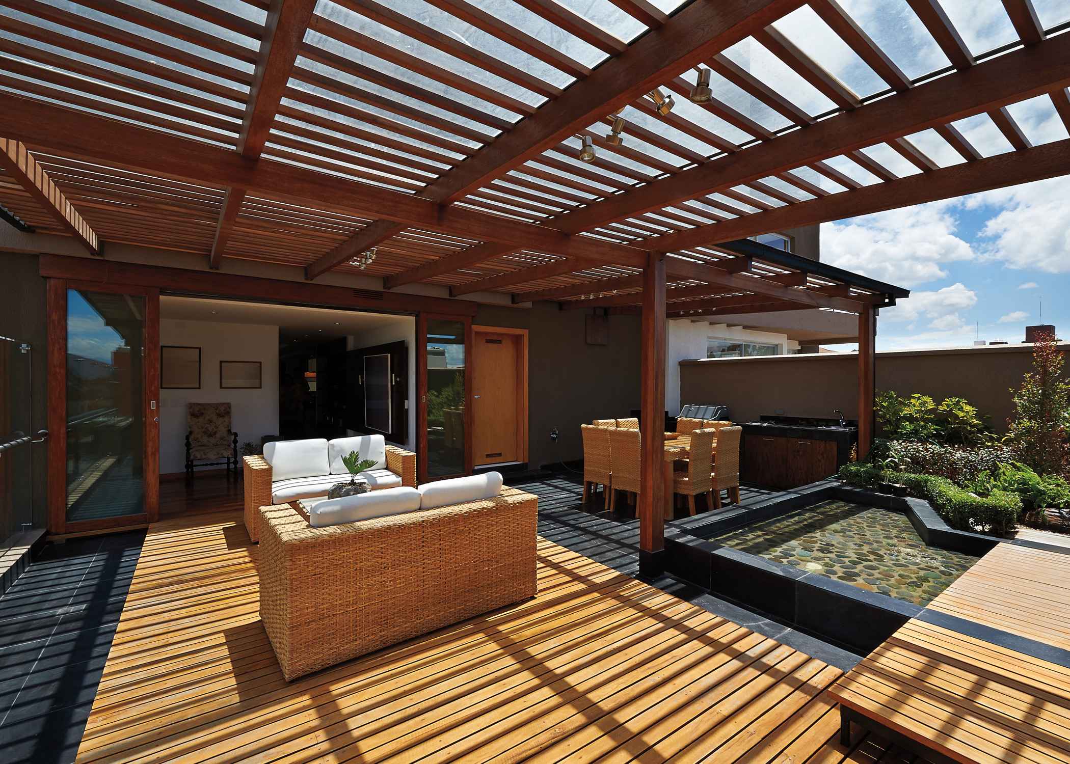 Sunny patio with modern wooden furniture and soft cushions surrounded by lush greenery.