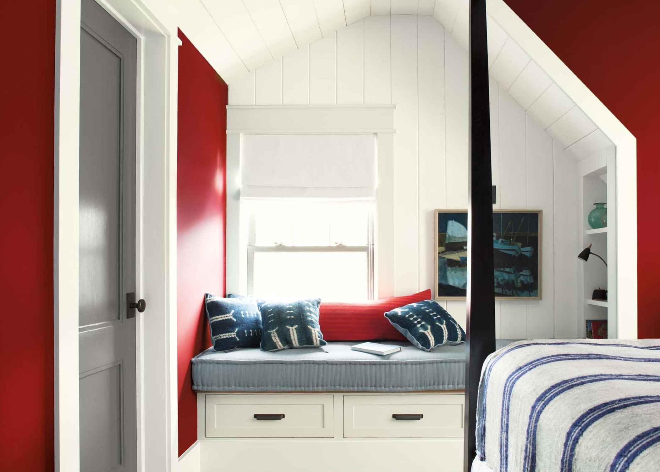 Cozy window seat with blue and red pillows in a nautical-themed bedroom.