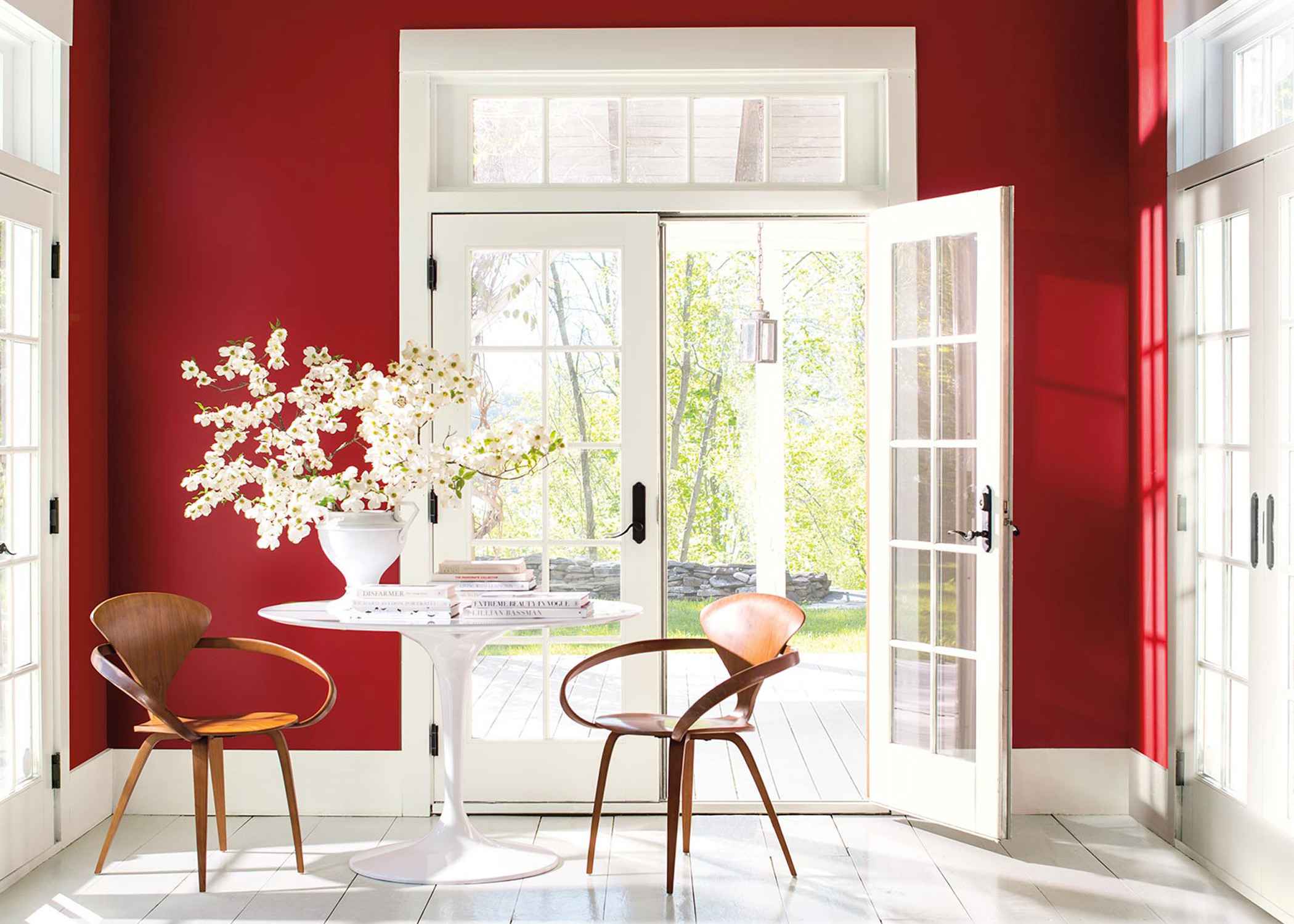 Bright room with bold red walls, French doors, and a white table topped with books and flowering branches.