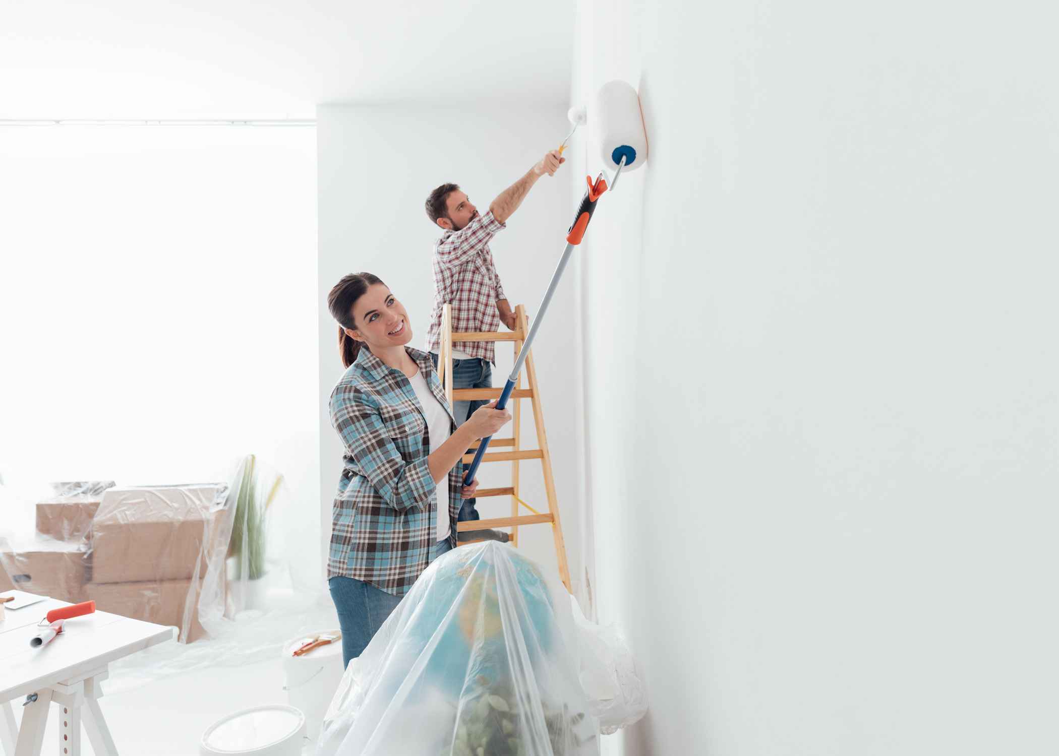 Couple painting a white wall, one on a ladder and one using a roller.