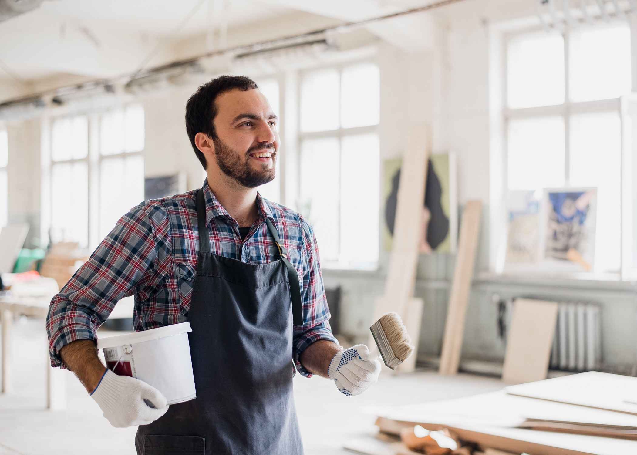 Smiling man in an apron holding a paintbrush and bucket.