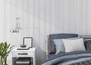 Modern bedroom with vertical striped wallpaper, navy and gray bedding, and a white nightstand topped with books, a bowl, and framed art.